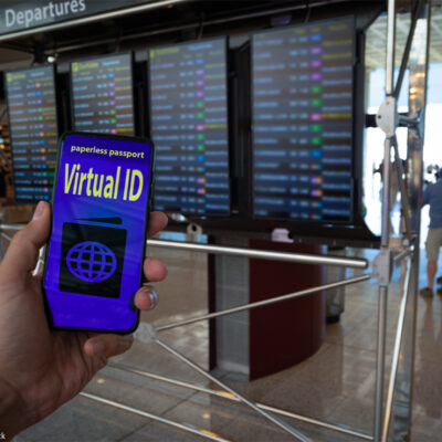 Hand holding a paperless passport virtual ID on smartphone screen with airport timetables as background.