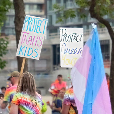 A person holding a sign with the text: Protect Trans Kids, during the pride parade.