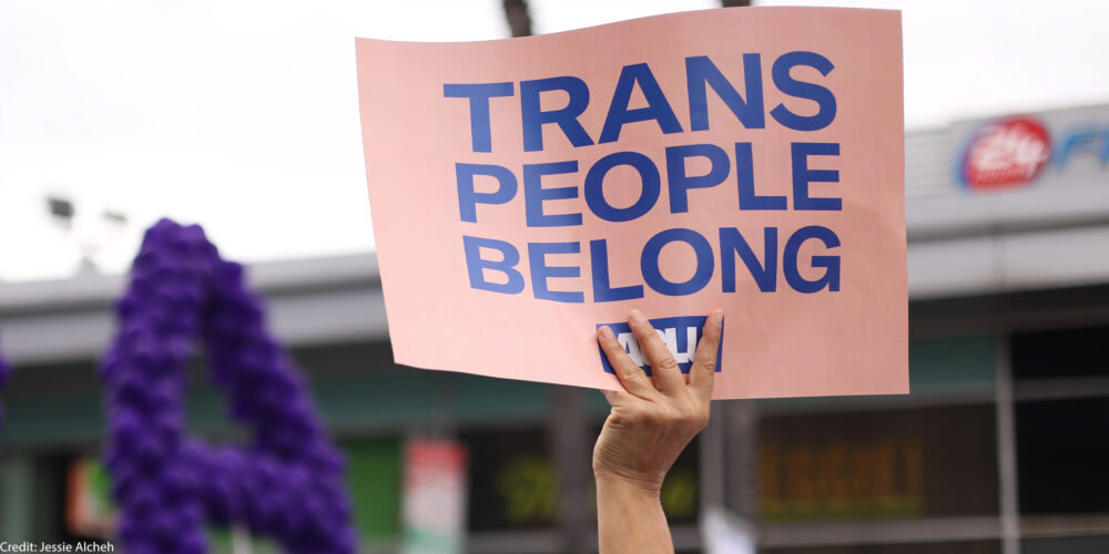 Someone holding a sign that says "Trans People Belong."