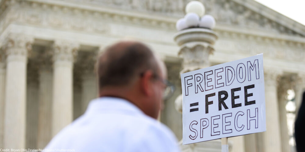 Someone holding a sign that says 'Freedom = Free Speech'