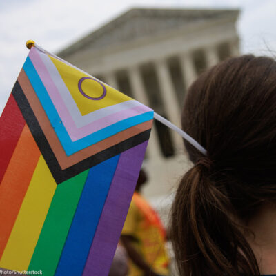 A Pride supporter (whose face cannot be seen) holds an Intersex-inclusive Pride Flag in their hair while facing the Supreme Court.