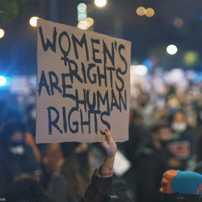 A sign reading "WOMEN'S RIGHTS ARE HUMAN RIGHTS" is held high by women's rights advocates.