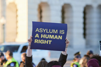 Asylum supporter holding up a sign reading " ASYLUM IS A HUMAN RIGHT".