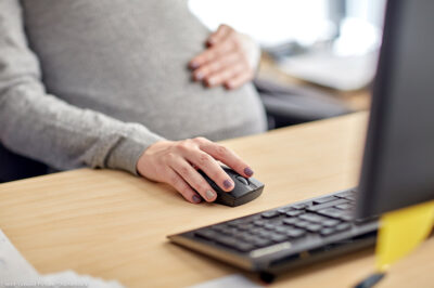 A pregnant worker on a computer at her desk.